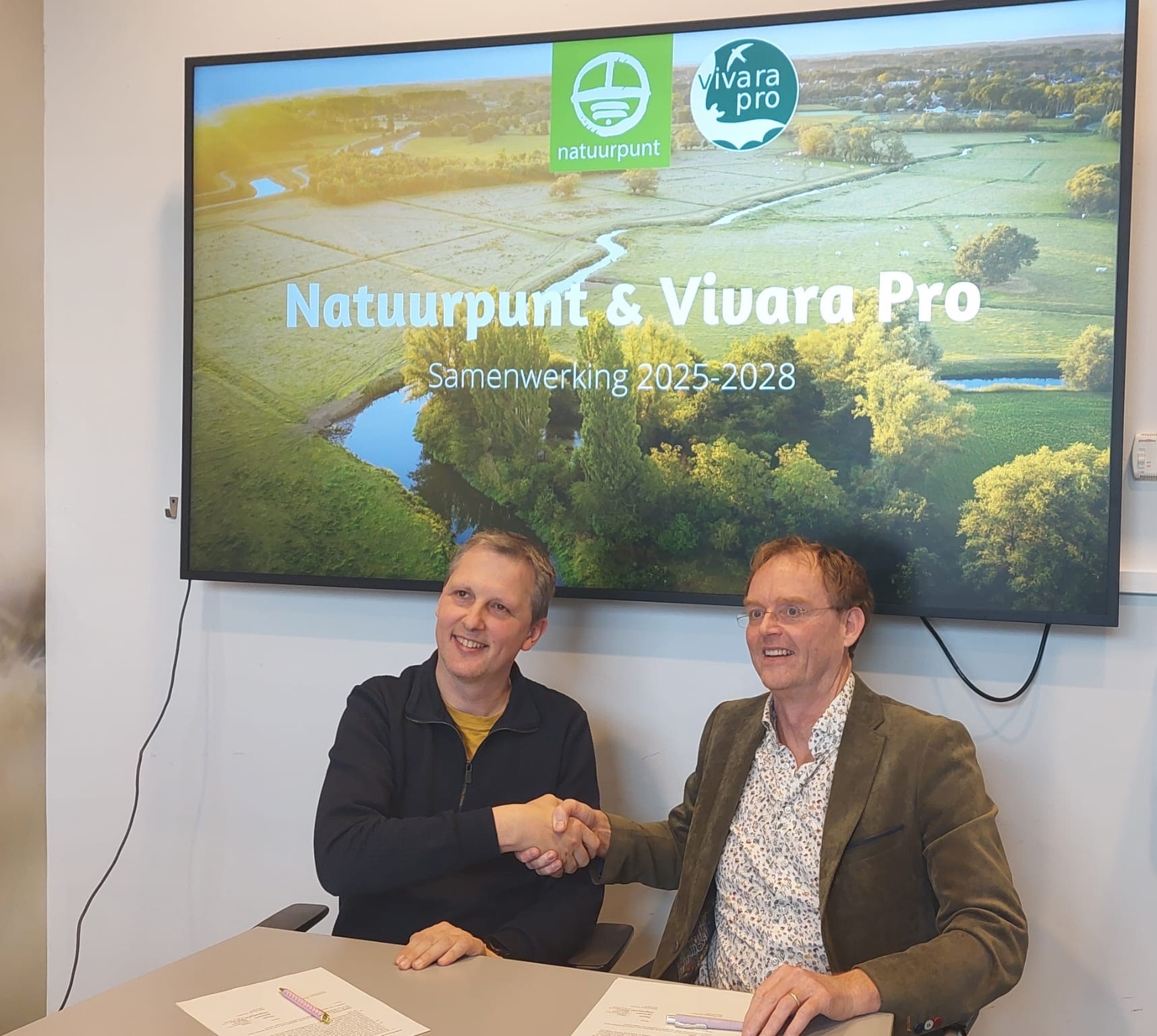 Natuurpunt_Vivara_Pro Afbeelding waarin de directeur van Natuurpunt, Noah Janssen en de directeur van Vivara Pro, Jan Thomassen elkaar de hand schudden en een samenwerkingsovereenkomst tekenen.
